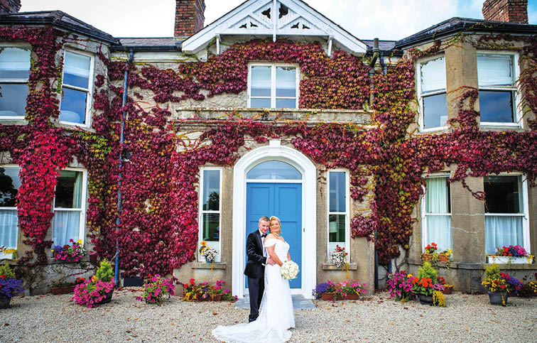 A bride and groom standing in front of a house with a purple door. Description generated by AI