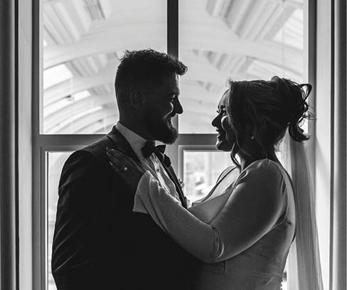 A man and woman are standing in front of a window. Description generated by AI