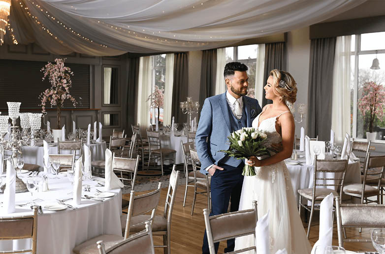 A bride and groom standing in front of a table with a vase of flowers. Description generated by AI