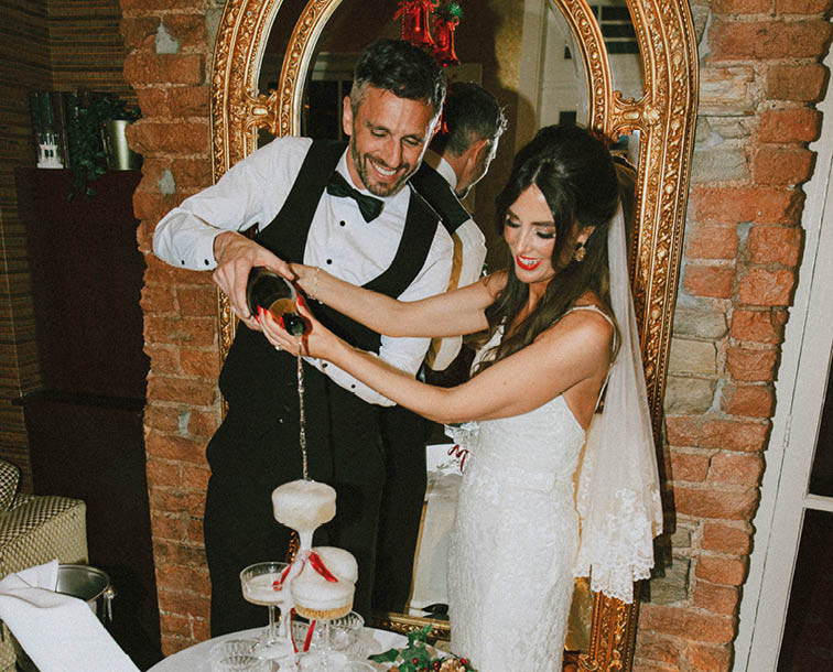 A man and woman are standing in front of a table with a drink and a cake. Description generated by AI