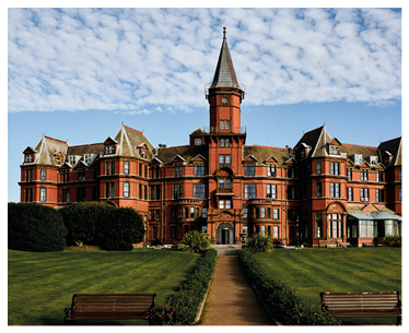 A large red building with a clock tower and a green lawn. Description generated by AI