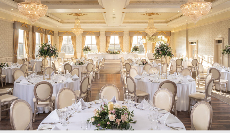 A large room with a long table set for a wedding reception. Description generated by AI