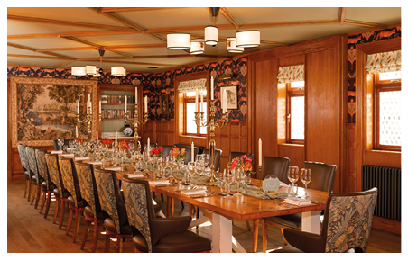A long wooden dining table with a white tablecloth and place settings. Description generated by AI