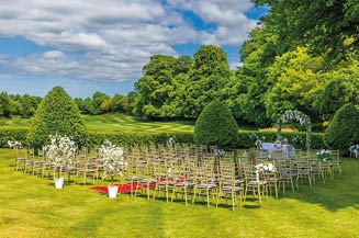 A green field with white flowers and chairs set up for a wedding. Description generated by AI