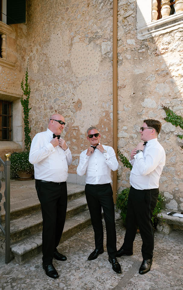 Three men wearing white shirts and black pants standing in front of a building. Description generated by AI