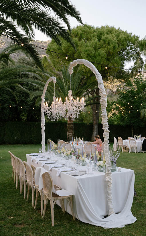 A long white table with a white tablecloth and place settings. Description generated by AI
