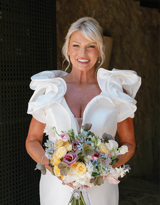 A woman wearing a white dress and holding a bouquet of flowers. Description generated by AI