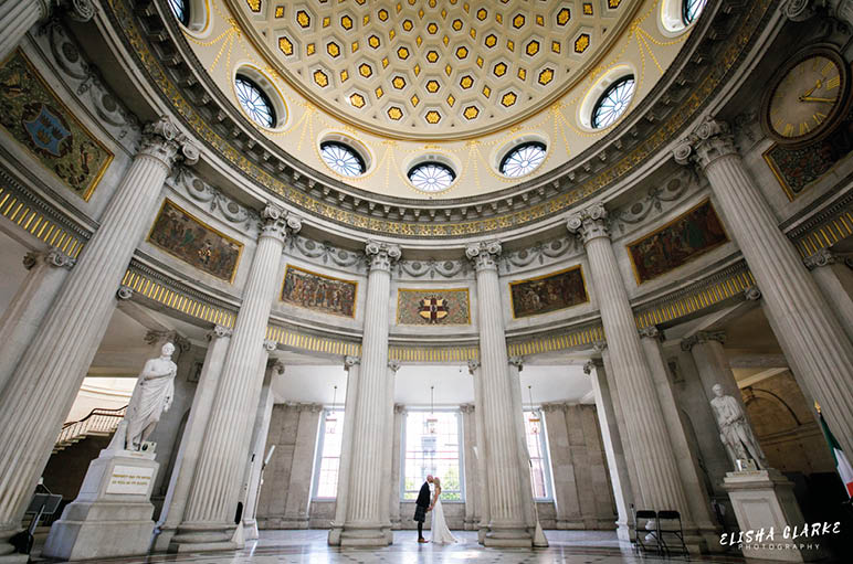 A man is standing in a large, open, and ornate room with a dome ceiling. Description generated by AI