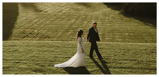 A bride and groom walking on a grassy field. Description generated by AI