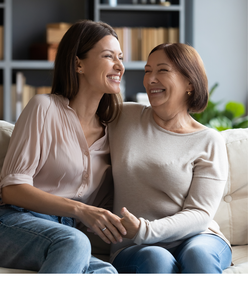 Overjoyed young woman with mature mother chatting, laughing at joke, enjoying pleasant conversation, middle aged mum and grownup daughter hugging, having fun, sitting on cozy couch at home