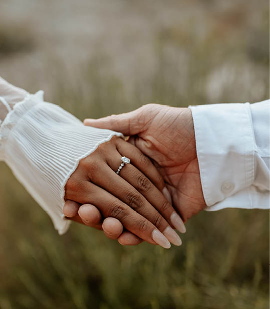 Hands close-up of boho couple in nature holding hands and walking, hugging having fun for their engagement photo session.