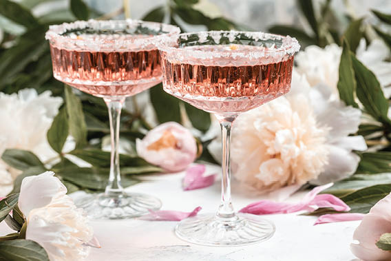 Rose wine in glass and peony flowers over white background, Summer celebration, wedding greeting card, invitation concept.