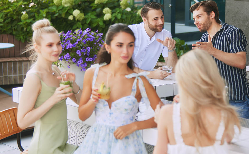 Friends enjoy drinks, women engaged in conversation man talking with male bartender. Atmospheric outdoor bar. Concept of friendship, party, leisure, celebration, relaxation