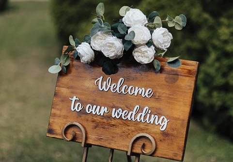 Wooden board with welcome sign on it decorated with white flowers in the garden.