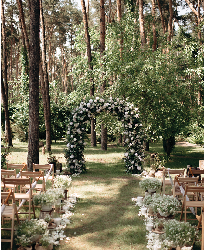 Natural minimalist wedding decor of white flowers and greenery on a green lawn with wooden chairs