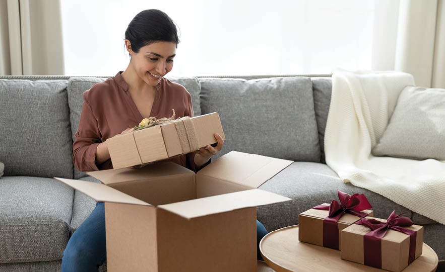 Smiling attractive young indian ethnicity woman unpacking huge cardboard box with wrapped gifts, feeling excited of winning prizes or preparing surprises for family for special event celebration.