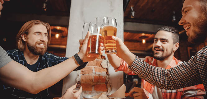 Four friends, young bearded men modern clothes, raised their glasses up, clinking and laughing in pub. Concept of male friendship