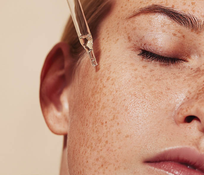 Close-up highly detailed shot of female skin with freckles and pipette with serum. Cropped shot of young woman with smooth perfect skin applying liquid serum on face.