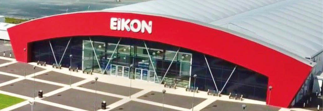 A modern building with a curved red facade and large glass windows displays the word EIKON above the entrance. Description generated by AI