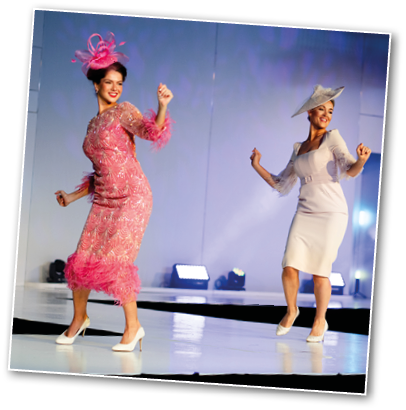 A person wearing a light-colored dress and matching hat is joyfully dancing on a brightly lit stage. Description generated by AI