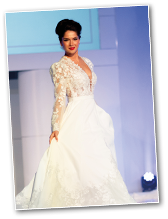 A person wearing a white wedding dress with a lace floral bodice and long sheer sleeves is holding the skirt while standing against a light background. Description generated by AI