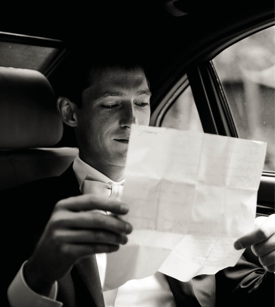 Groom reads his wedding speech sitting on the back seat in the car