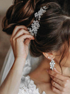 The hairdresser makes a fashionable and stylish styling on the bride's hair. Beautifies a hairdress with a beautiful precious accessory made of white beads