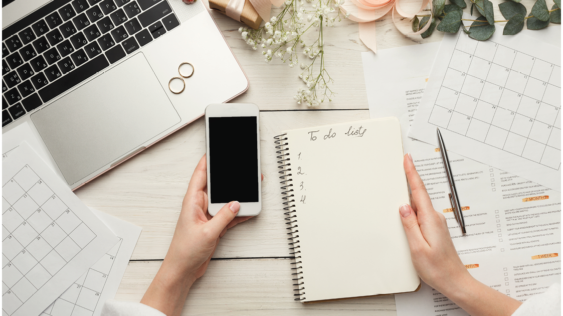 Wedding arrangement background. Female hands preparing for marriage, using laptop, smartphone, paper calendars and planners, top view. Bridal wallpaper with copy space on to do list