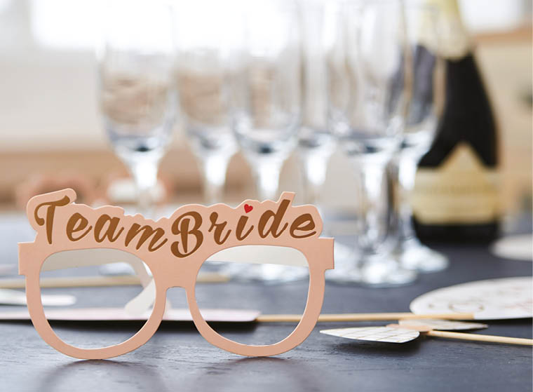Theme paper glasses with “Team Bride" sign on a grey table with wineglasses with champagne. Bachelorette hen party decorations in light room. Party time. Bridal shower. 
