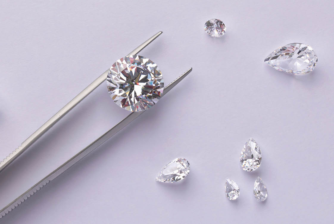 Layout of round cut diamond on tweezers with other diamonds of different cuts on light background with copy space top view.