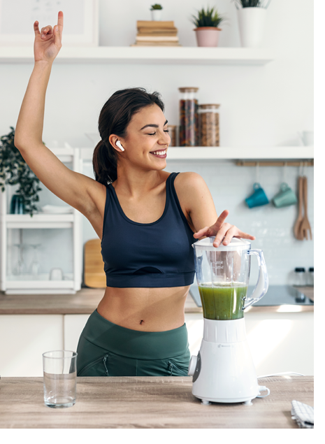Shot of athletic woman preparing smothie while singing, dancing and listening music with earphones in the kitchen at home.