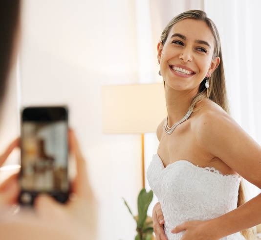 Smartphone photography of woman with wedding jewelry for luxury, fashion and wealth with smile portrait in a boutique or hotel. Bride in white dress with diamond or silver necklace for social media