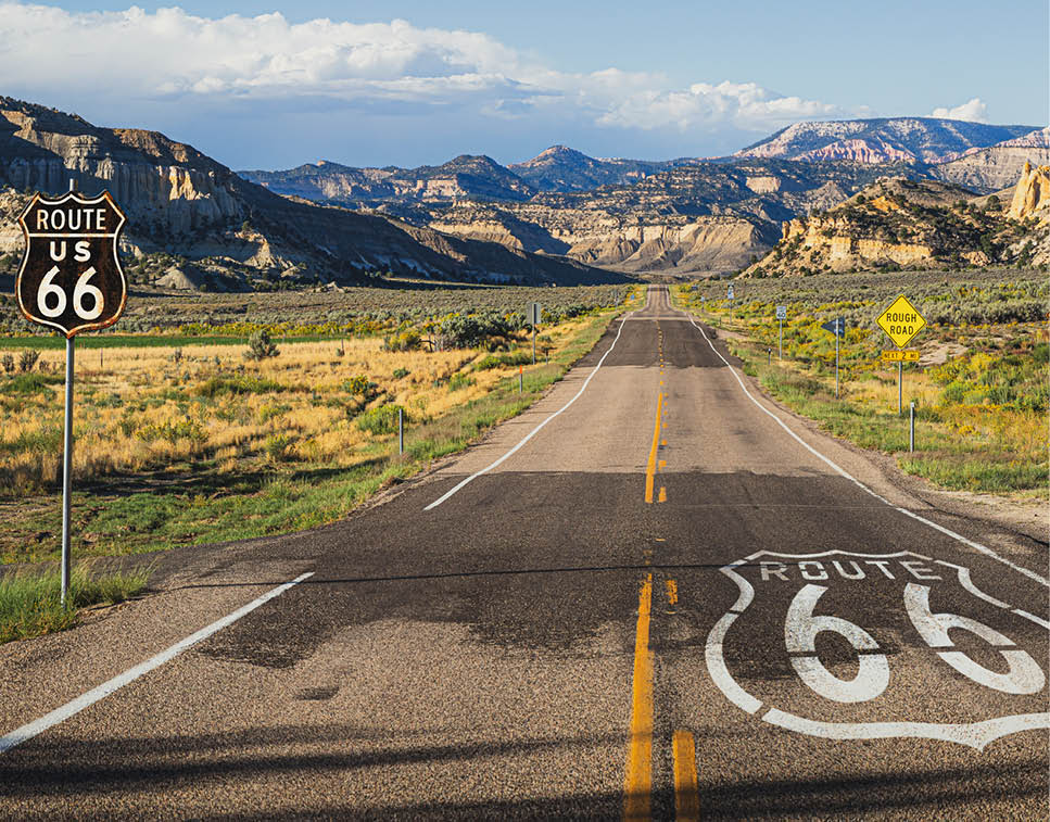 Scenic panoramic view of long straight road on famous Route 66 with historical street signs and paintings in classic american wild western mountain scenery in beautiful golden evening light at sunset