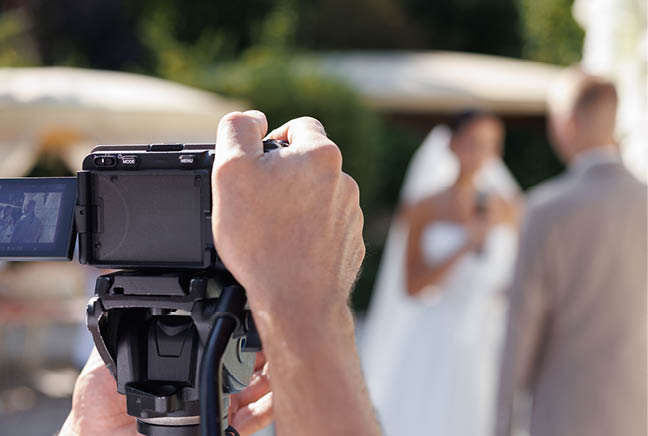 A cameraman filming a wedding ceremony with a camera on a tripod