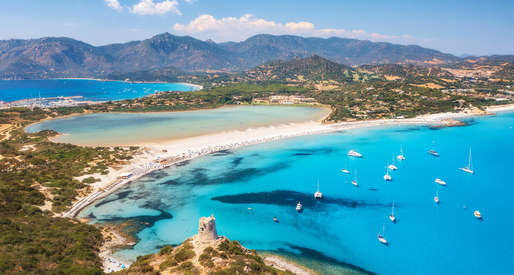 Aerial view of beautiful sandy beach, old tower on the hill, sea bays, mountains at summer sunny day. Porto Giunco in Sardinia, Italy. Top view of blue sea with clear water, white sand, mountains