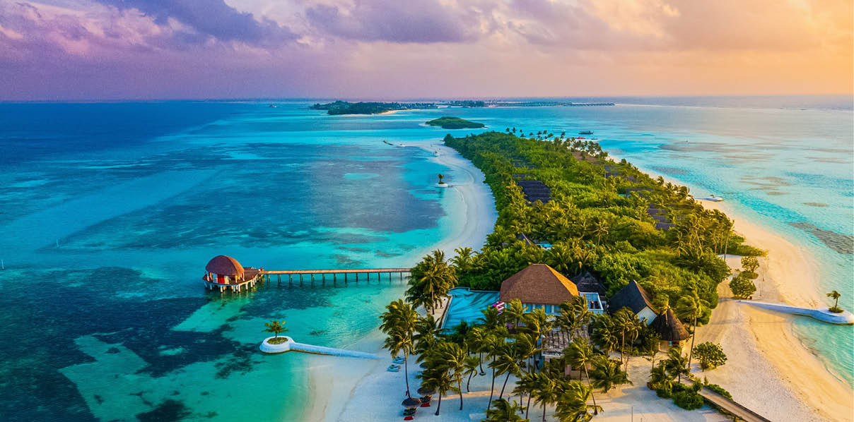 Tropical paradise aerial view of a luxury island resort in the Maldives at sunset with turquoise lagoon, white sand beaches, lush palm trees and overwater villas.