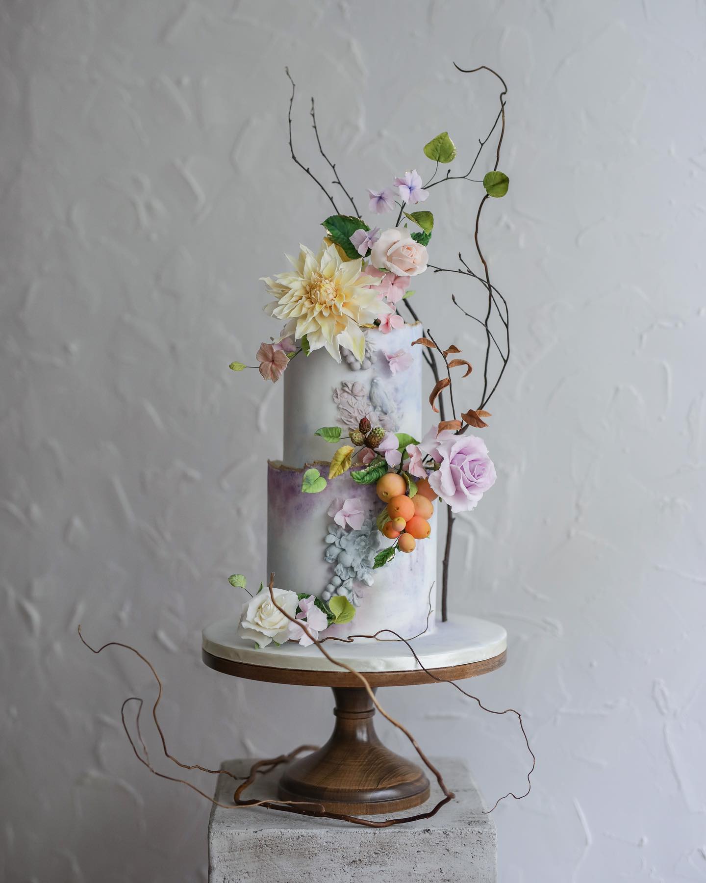 This two tiered cake has a purple marble effect and an array of colour flowers, fruits and foliage as decoration.