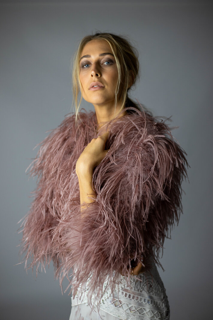This image shows a young women wearing a dramatic bolero made of feathers. This is a feathery cover-up.