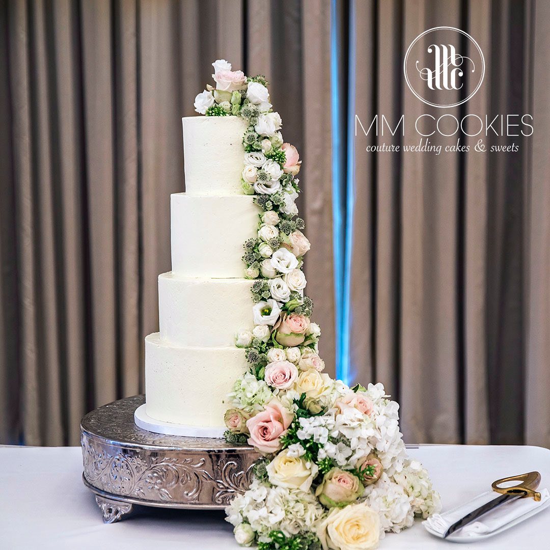 A wide four tiered wedding cake with an array of flowers flowing from top to bottom.