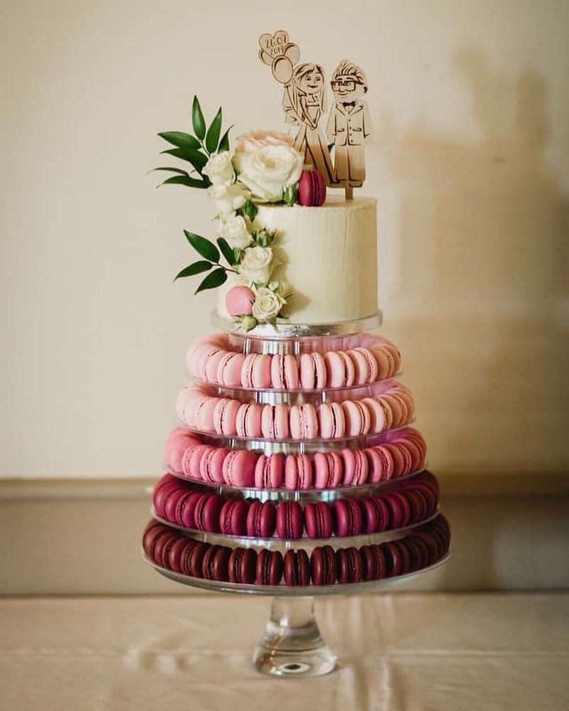 This image highlights a Macaron Tower consisting of different purple hues. A small wedding cake sits on top of this tower. Image used in the 6 Wedding Cake Trends of 2022.