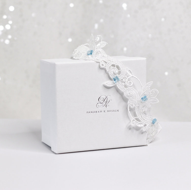 A white bridal garter with pops of blue. Image used in the 8 Unique Something Blue Ideas For Your Wedding Day.