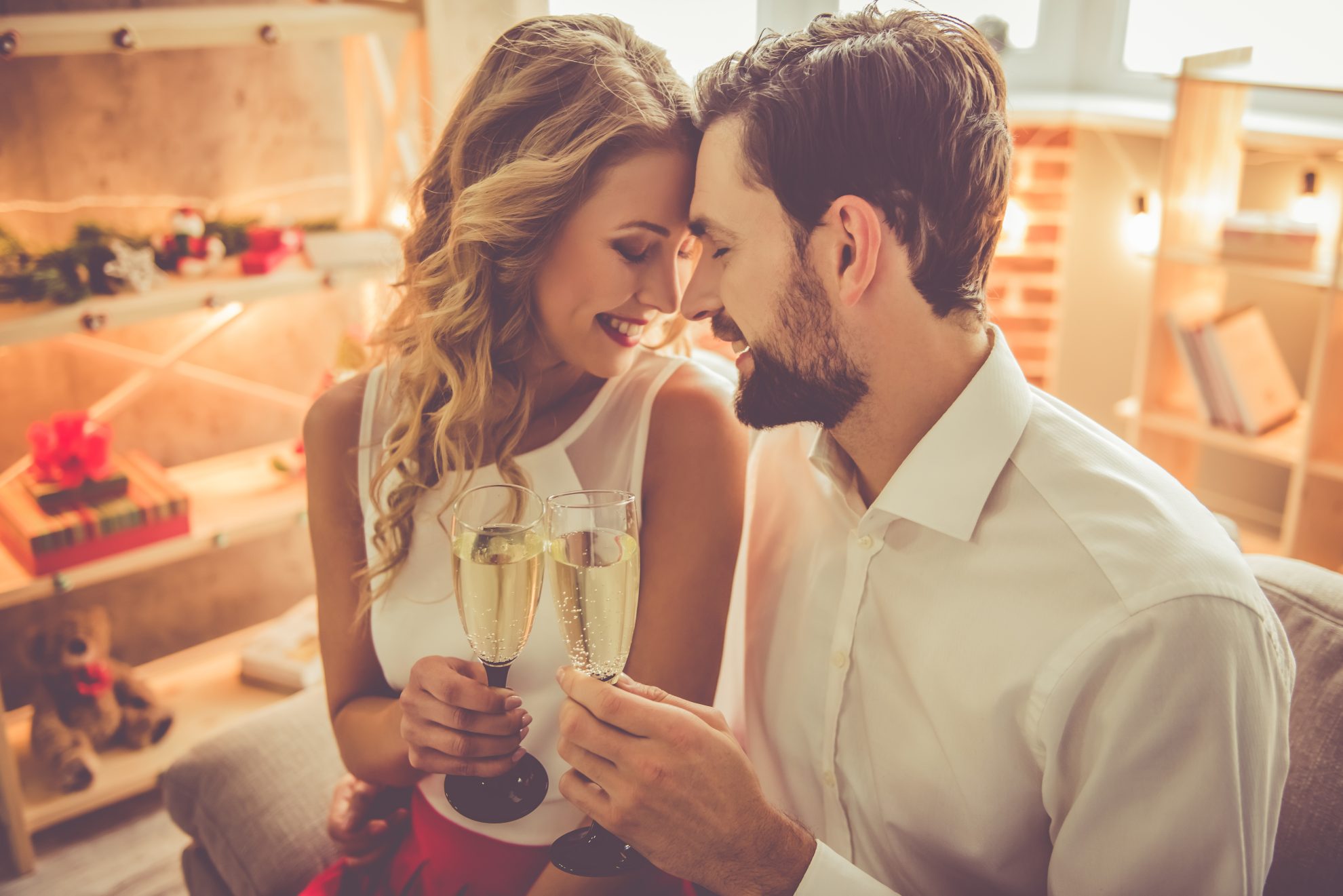 A man and women hold their heads close together and have a glass of champagne. Image used in the The Top 14 Things You Need To Do Once You're Engaged article. 