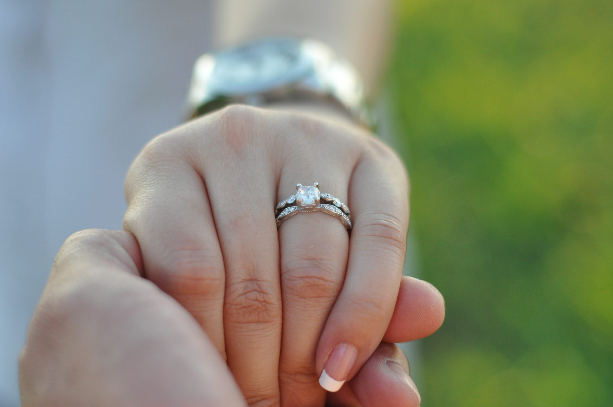 The image shows a lady holding a man's hand showing off her engagement ring. Image used in the The Top 14 Things You Need To Do Once You're Engaged article. 