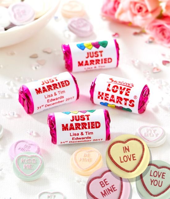 Four mini packets of Swizzel's Love Hearts are on a table with confetti around them. Image used in the Cute Wedding Favours Your Guests Will Want To Take Home article. 
