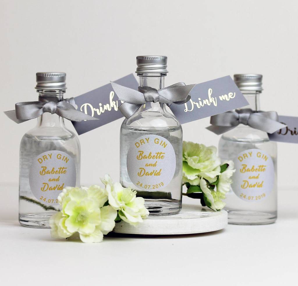 Three small bottles of dry gin with the name of the couple and the date they got married sit on the table. A silver bow is around the neck of the bottle along with a label saying Drink Me.