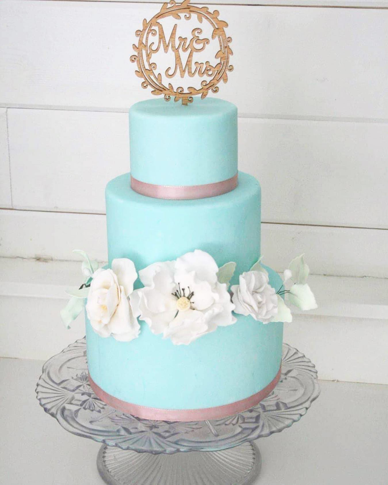 A three tiered wedding cake. This is a blue wedding cake with pink ribbons and white flowers on it.