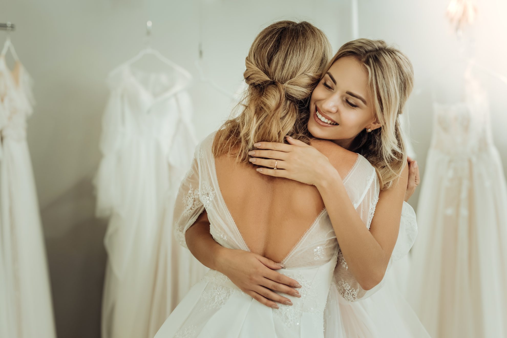 A bridemaid hugs a bride in a wedding dress shop. Image used in the Maid of Honour Duties : The Ultimate Guide article.