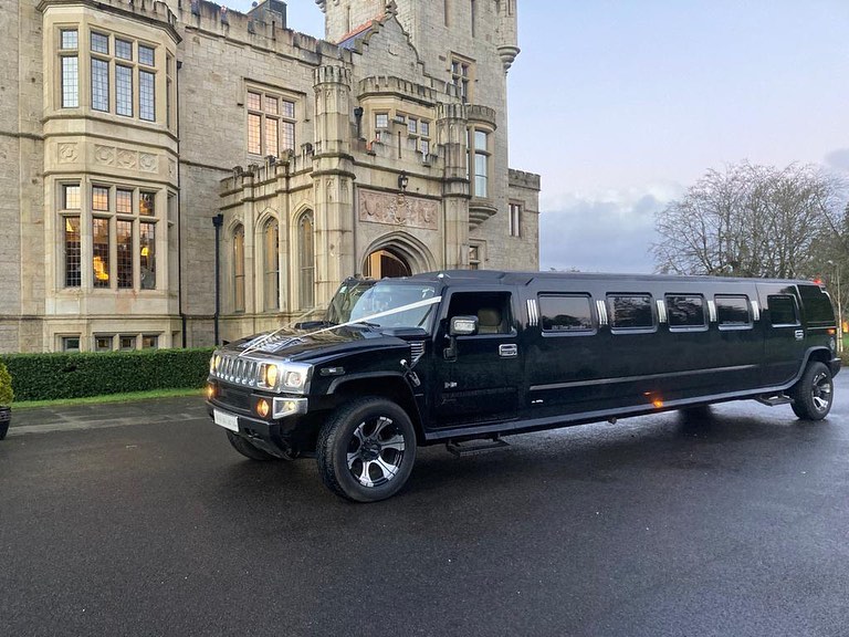 A black hummer limo with wedding ribbons parked outside a wedding venue. Image used in the What Type Of Wedding Transport Suits Your Personality article.