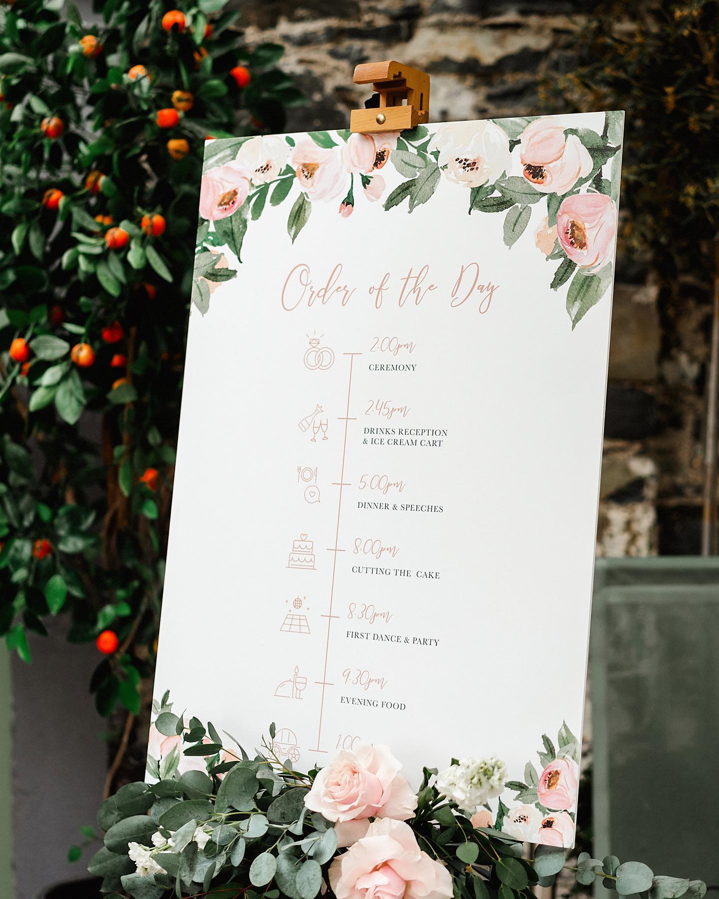 This wedding welcome sign highlights the order of the day from the time of the ceremony to closing time. Pink flowers and green foliage can be seen at the bottom of the sign and complements the drawn roses and foliage at the top of the sign.