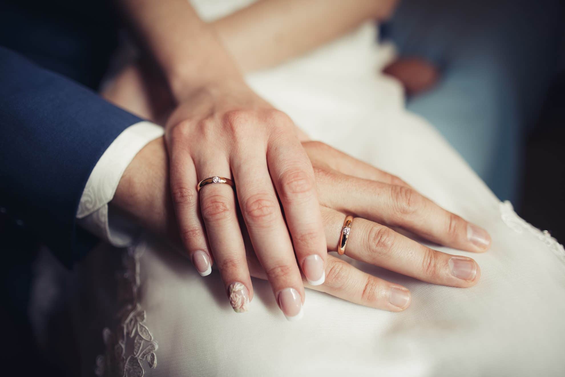 A bride places her hand on top of the groom's hand, displaying their wedding rings.